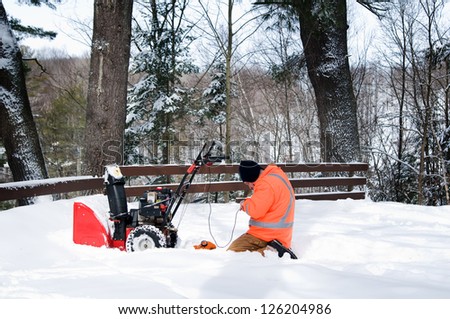 man outdoors in the snow fixing a snow-blower