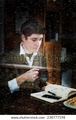 man drinking coffee in a cafe shot through a rain covered window