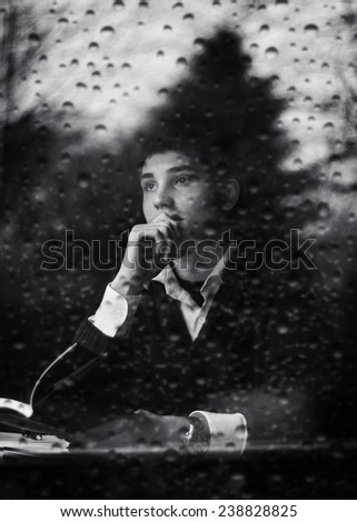 black and white of a man lost in thought in a cafe. Shot taken through a rain covered window
