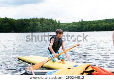 young boy wearing a life jacket paddle boarding on a lake