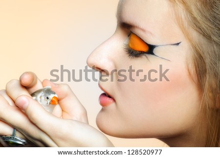 Beautiful girl with creative makeup and bird in her hands