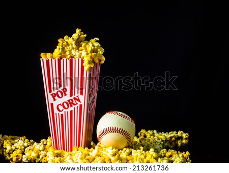 A close up shot of a classic box of red and white striped popcorn box with a baseball isolated against a black background.