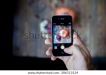 man taking a photo with his smart phone of organic pomegranate open cut in half and full one on a wooden dark table background decorated in rustic style