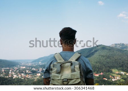 handsome man guy tourist standing alone by the mountain forest landscape during his summer vacation with his backpack back view