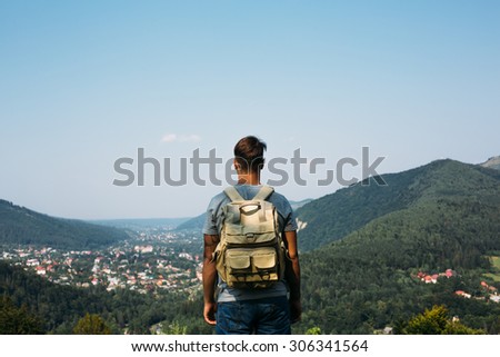 handsome man guy tourist standing alone by the mountain forest landscape during his summer vacation with his backpack back view