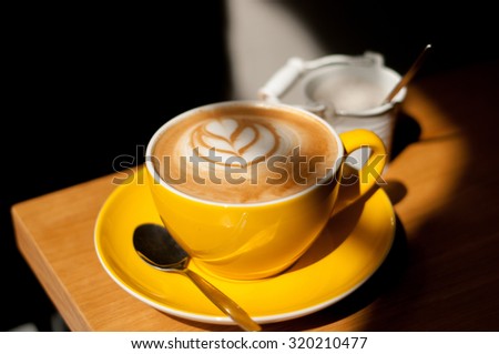 cappuccino with heart in yellow cup on wood table background overhead view cool shadows natural light