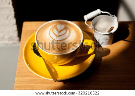 cappuccino with heart in yellow cup on wood table background overhead view cool shadows natural light