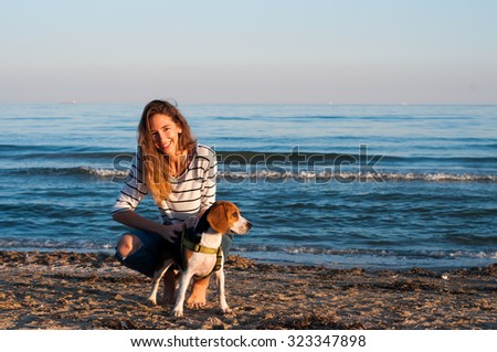 cool trendy stylish sexy blonde happy girl having fun playing with her beagle puppy dog on the beach sea background