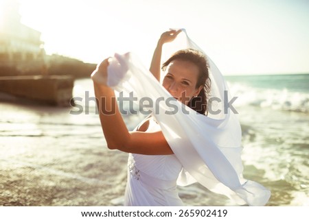 happy beautiful bride walking on the beah holding veil
