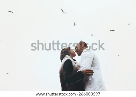 stylish beautiful happy bride and groom kissing on background cloudy sky and flock of birds in Lyon with goblet in hand