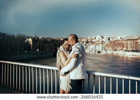stylish beautiful rich bride and groom hugging on a sunny day on the bridge in the city Lyon on a background of the river and city