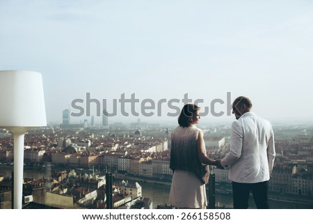 wonderful rich bride and groom look at each other holding hands on the terrace on the background of blue sky Lyon city