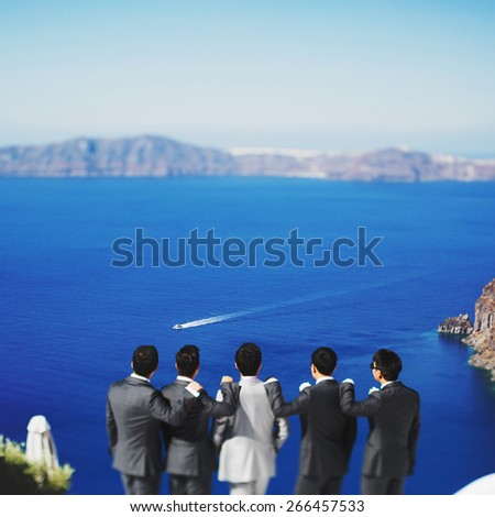 stylish rich asian groom with s?hafer and best men watching the blue sea on the island of Santorini before wedding ceremony