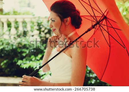 amazing beautiful rich stylish smiling bride under red umbrella  background wall columns and leaves