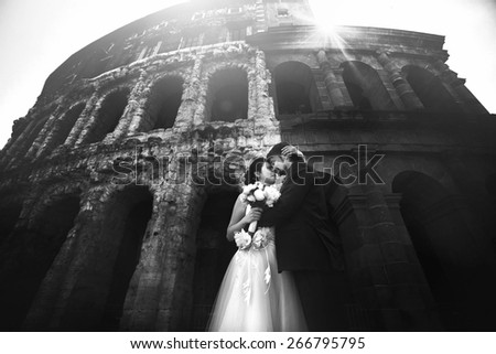 Stylish rich adorable bride and groom kissing on the streets of Rome Italy on a sunny day background Coliseum black and white