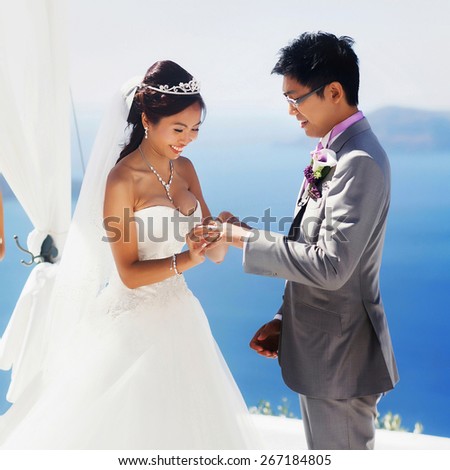 stylish rich asian bride and groom puts ring  wedding  on the island of Santorini, Greece sunshine