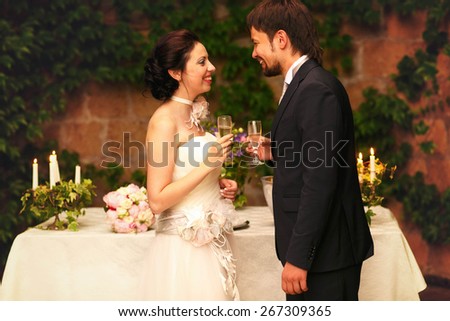 rich stylish happy bride and groom smiling  holding goblets with champagne  near a white wedding table decorated with flowers peonies and candles Rome Italy