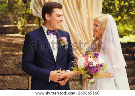 wonderful stylish rich happy bride and groom holding hands at a wedding ceremony in  garden near arch with flowers