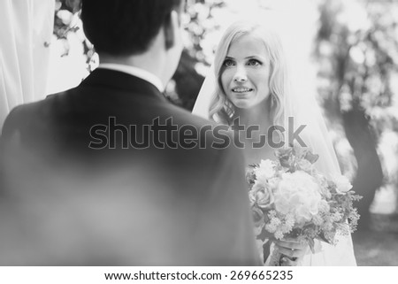 wonderful stylish rich happy bride and groom holding hands look et each other at a wedding ceremony in  garden near arch with flowers