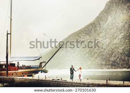 Stylish young bride and groom runing on the pier near yacht on background sea and mountains of Montenegro