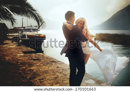 Stylish young bride and groom walking on the pier near yacht on backfround sea and mountains of Montenegro