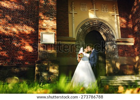 bride and groom walking kissing near trees and church