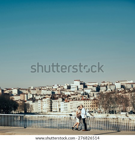 stylish beautiful rich bride and groom walking on a sunny day on the bridge in the city Lyon on a background of the river and city