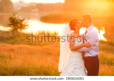 groom  and  bride is hugging and kissing on the background beautiful sunset on the lake