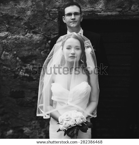 happy gentle stylish groom and bride are posing on the background old door and rock wall