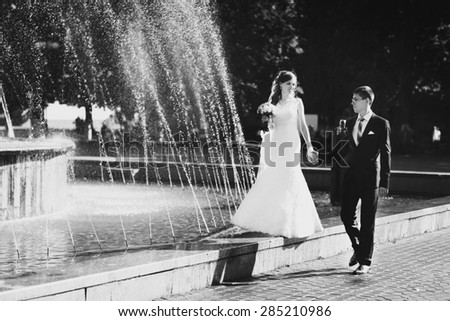 happy bride and groom walk near fountain