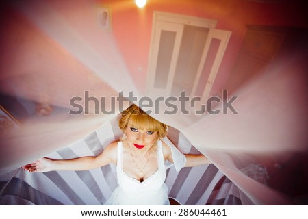 luxurious stylish smiling blonde bride with red lips is posing on the background of room