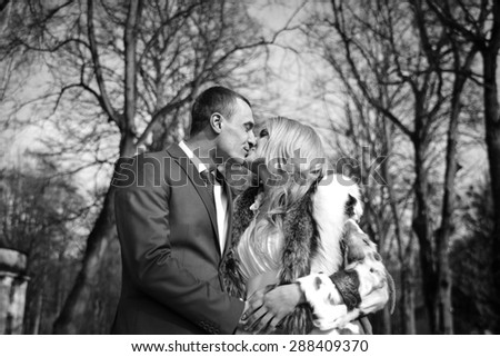 elegant groom hugging his stylish happy blonde bride and kissing on the background of park