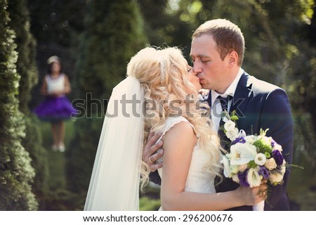 elegant stylish groom with his happy gorgeous blonde bride on the background of trees in the park