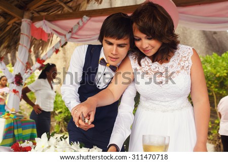 elegant gorgeous bride and groom  in the tropical bungalow cutting wedding cake, hawaiian decor, on the background of  the ocean and a beach, wedding ceremony in Seychelles