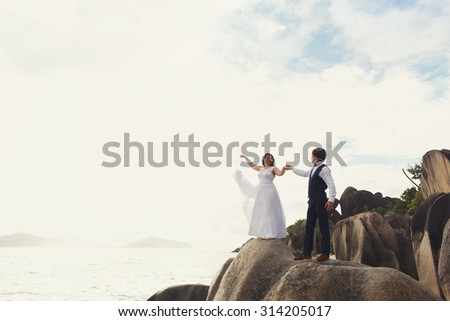 elegant gorgeous bride and groom walking on the beach on the background of the ocean and rocks, wedding ceremony in Seychelles