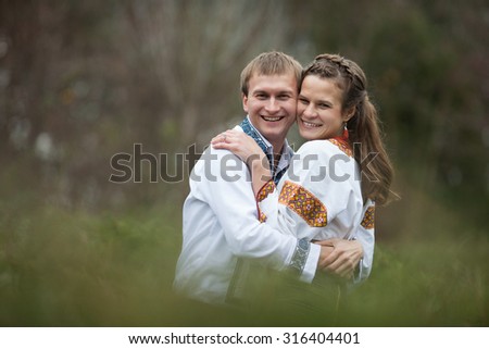 beautiful ukrainian bride and groom in native embroidery suits smiling on the background of trees in a park, traditional wedding ceremony