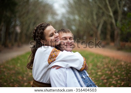 beautiful ukrainian bride and groom in native embroidery suits hugging on the background of trees in a park, traditional wedding ceremony
