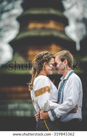 beautiful ukrainian bride and groom in native embroidery suits on the background of old church in autumn park