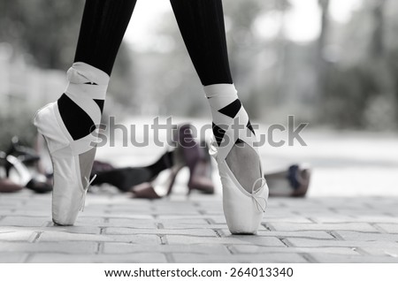 Closeup of a ballerina\'s feet in Pointe on the street, different kind of shoes in background