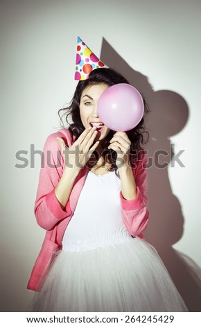 Young beautiful brunette woman in bright clothes celebrates her birthday with a pink balloon