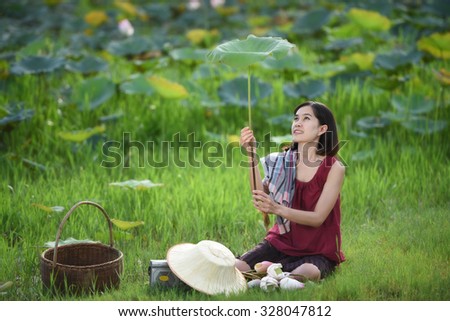 Young female ?farmer playing with lotus leaf and sitting near the pond