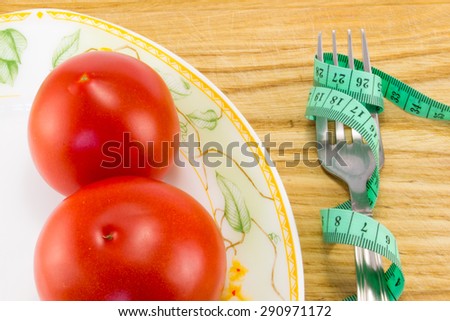 Measuring tape and a fork with tomato isolated on background, concept of healthy food and diet