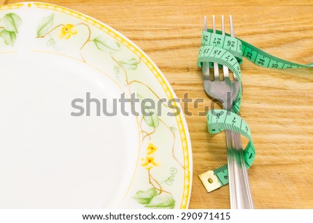 Empty plate with measure tape, knife and fork. Diet food on wooden table