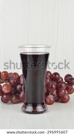 Glass of grape juice with grapes on the background.