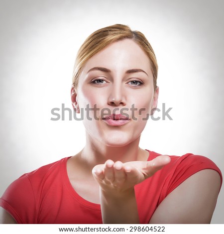 Attractive blonde woman blowing while sending an air kiss against a white background. Toned photo.