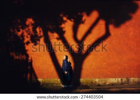loving couple standing on a background of orange wall and their shadow of tree falls on the wall