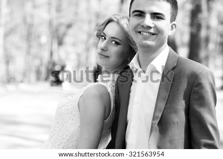 Black and white beautiful charming blonde bride and handsome groom in gray suit posing in park close-up