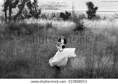 Black and white stylish happy bride running from elegant groom in rye field