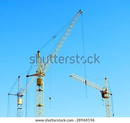 Three tall yellow lifting crane against the blue sky