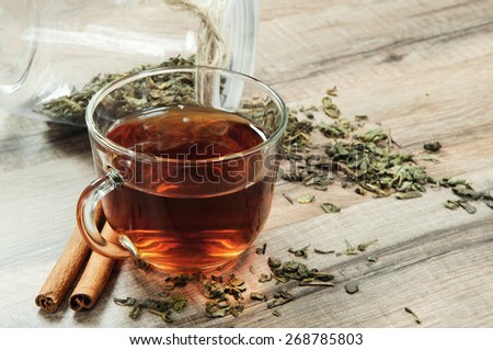 Black tea in a cup on a wooden table. next to a cup of tea, worth a bouquet of flowers of blossoming apricot, two cinnamon sticks and scattered dry tea leaves